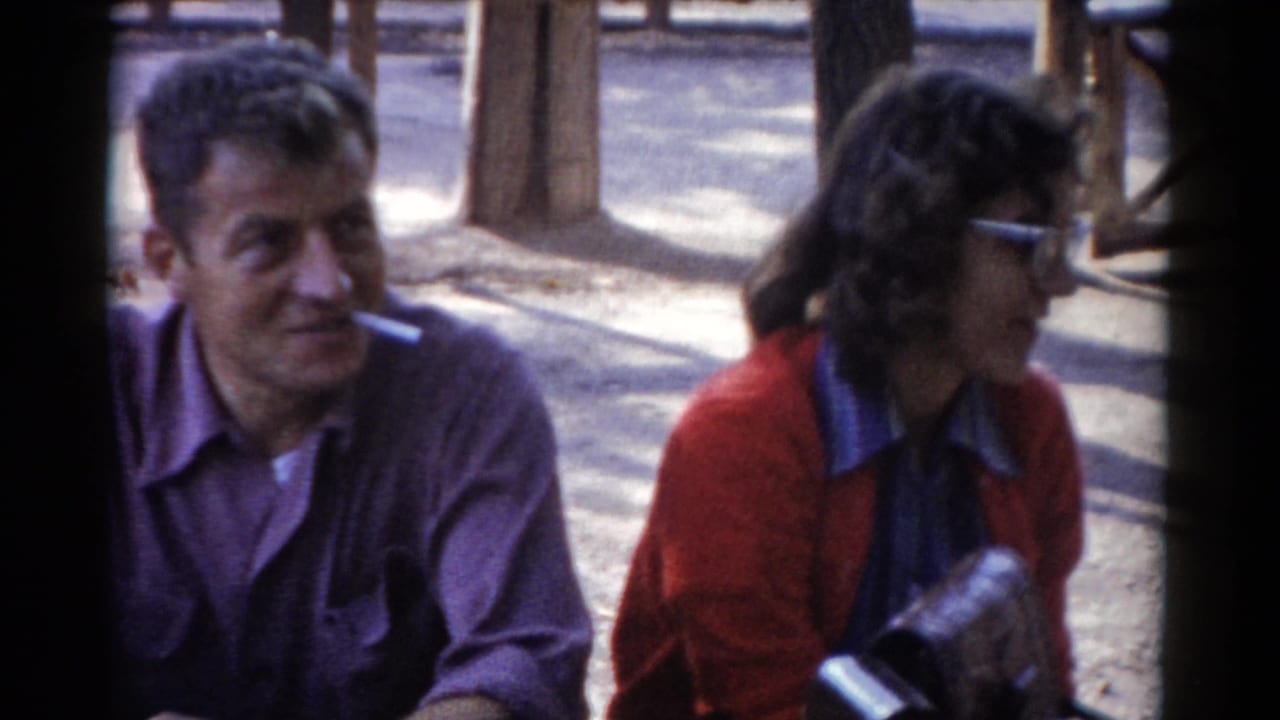 In the Catskill area in 1959, a seated man in a purple shirt smokes while facing a woman in a red cardigan and glasses.