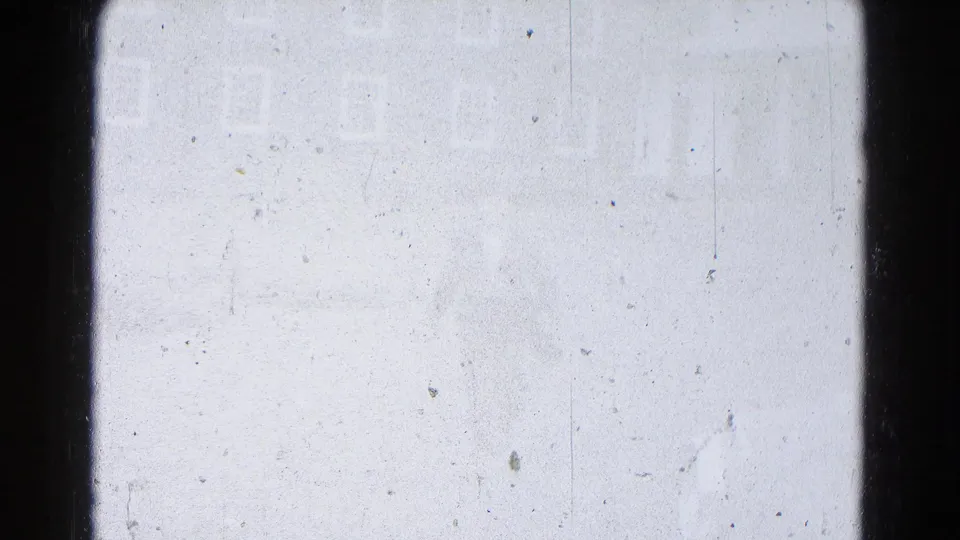 Overexposed 8mm home-movie frame with dust, scratches, dark side borders, and faint density changes but no identifiable person or building.