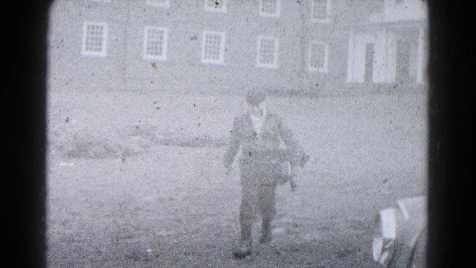 1959 Hagerstown home-movie frame showing a man walking across a yard toward the camera, with residential buildings behind him.