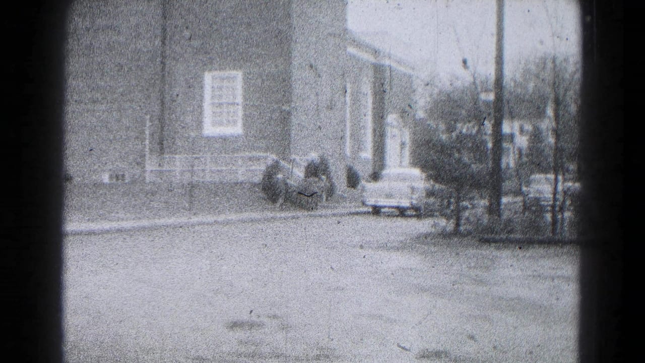 1959 Hagerstown street view with a brick building, white porch rail, parked car, and small group of pedestrians near the entrance.
