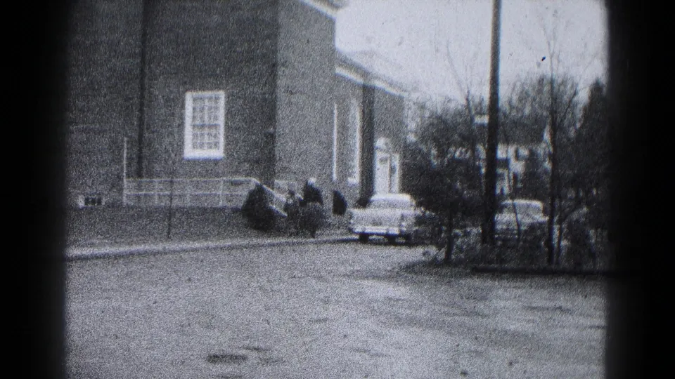 1959 Hagerstown street scene showing a brick residential-scale building, white railings, a parked car, and trees along the road.