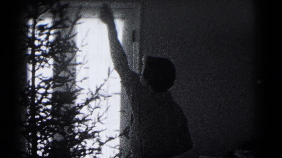 A family member in the 1959 Hagerstown home movie reaches up near the Christmas tree, backlit by a window.