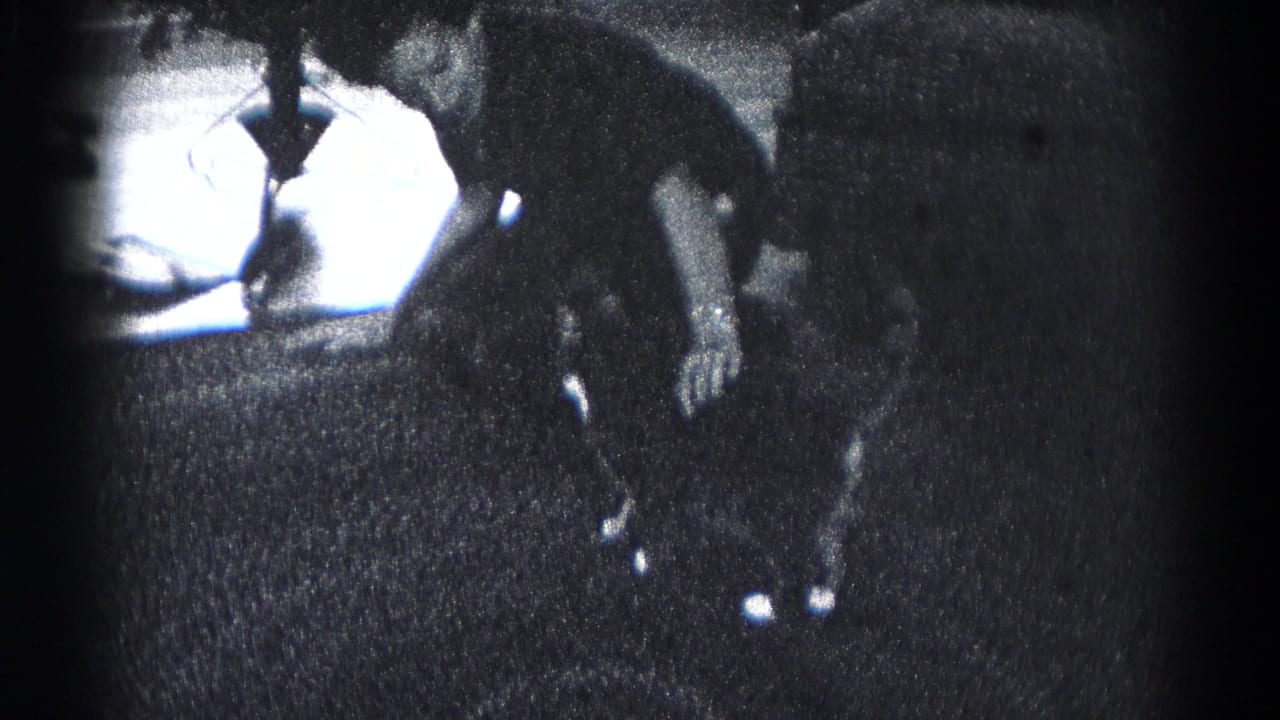Person bends near a small table in a dark interior with a potted plant nearby.