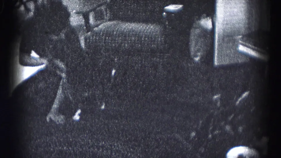 A person in dark clothing bends beside an upholstered chair and table area in the 1959 Hagerstown home-movie scene.