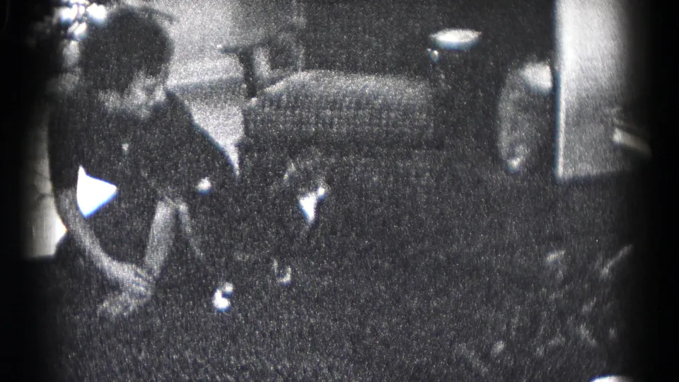 Inside the Hagerstown residence, an adult bends near plants and holiday items beside an upholstered chair in grainy black-and-white footage.
