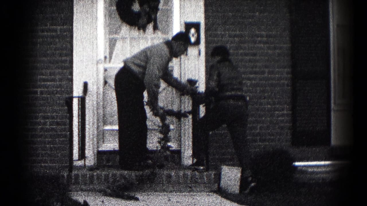 The father leans in to guide the younger person with the wreath at the brick home's entry in Hagerstown, Maryland.