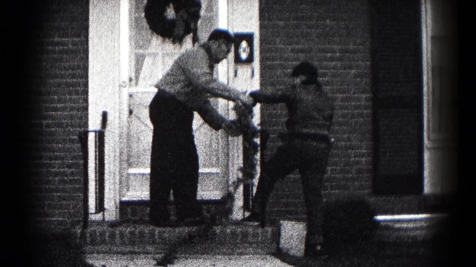 The pair adjust holiday greenery at the entrance, with the brick doorway and existing wreath visible in the 1959 home movie.