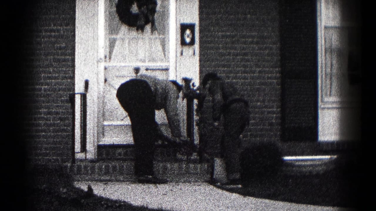 In 1959 Hagerstown home-movie footage, two men stand and bend near a flower pot at a brick home's front entrance.