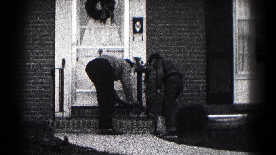 In 1959 Hagerstown home-movie footage, two men stand and bend near a flower pot at a brick home's front entrance.