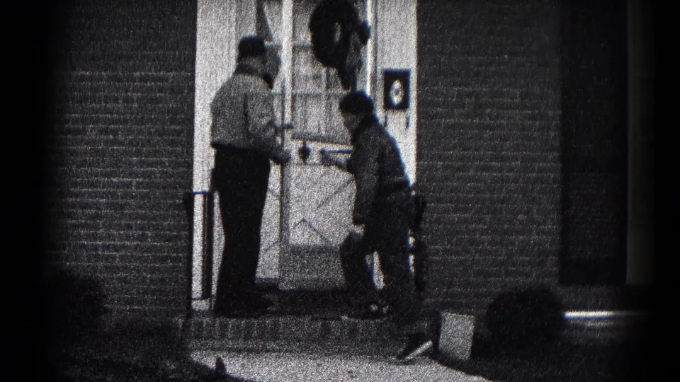 Two men in jackets appear to adjust a plant or pot at a brick front entrance in Hagerstown, Maryland, 1959.