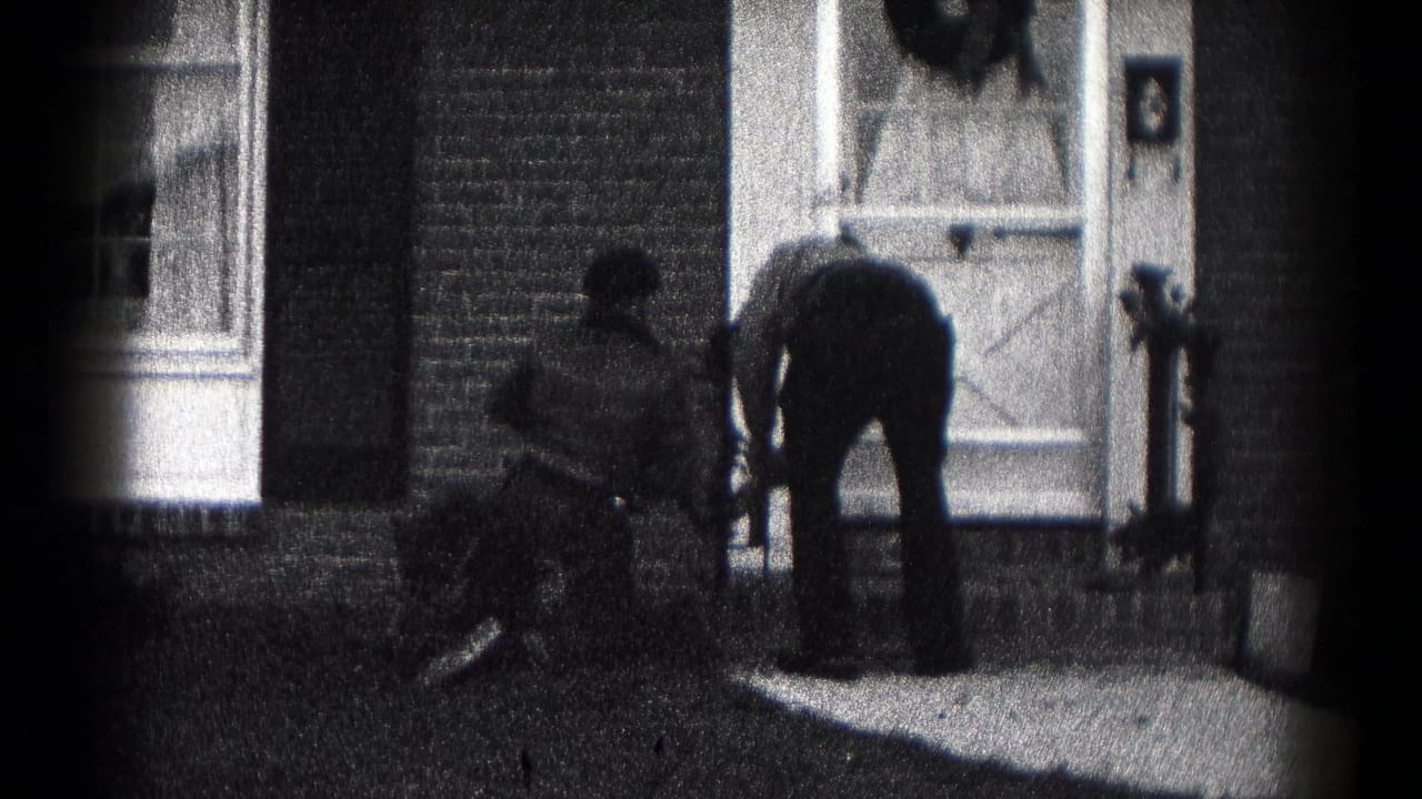 In 1959 Hagerstown home-movie footage, two figures bend near a brick house porch below a door with a Christmas wreath.