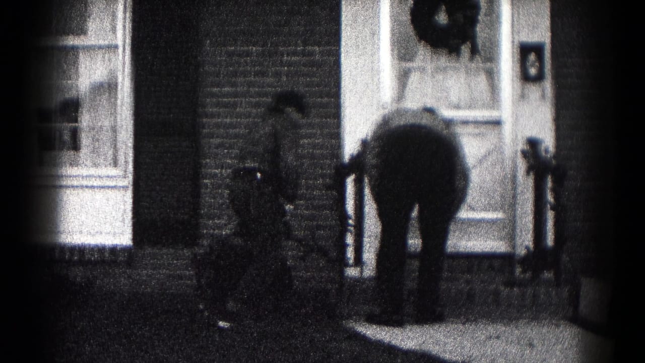 Black-and-white 8mm frame from Hagerstown shows one person bent at the porch and another nearby at a brick house entrance.