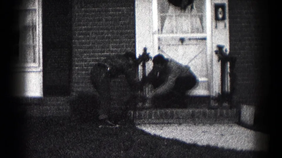 Two figures appear to adjust or repair something low on the porch railing beside a wreath-decorated door in Hagerstown.