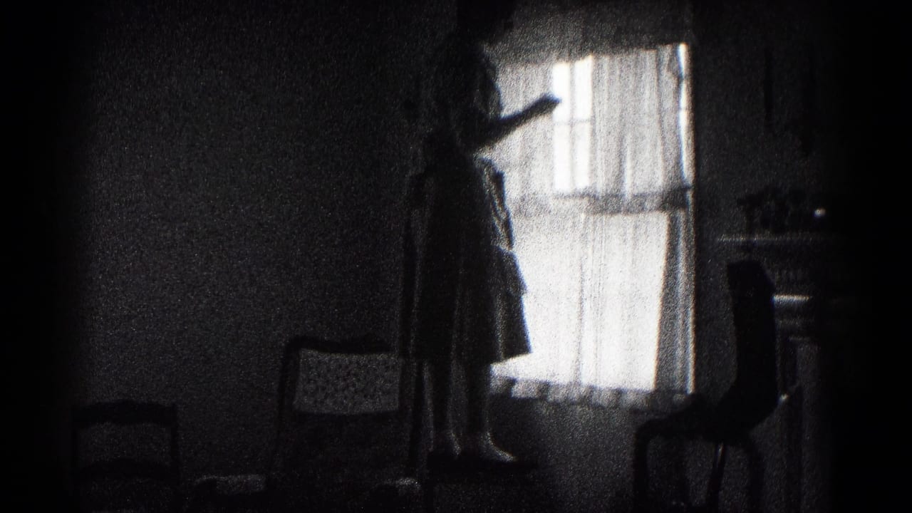 In a 1959 Hagerstown home-movie frame, a woman stands on a chair adjusting sheer curtains in a dark interior.