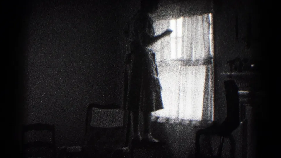 In a 1959 Hagerstown home-movie frame, a woman stands on a chair adjusting sheer curtains in a dark interior.