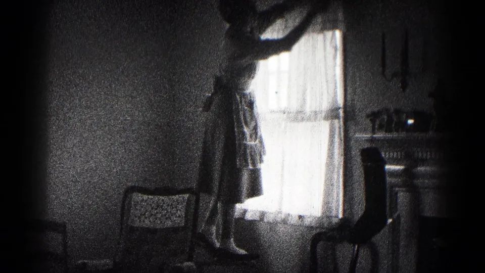 A grainy 8mm frame shows the woman on a chair reaching toward sheer curtains in a dim 1959 Maryland room.