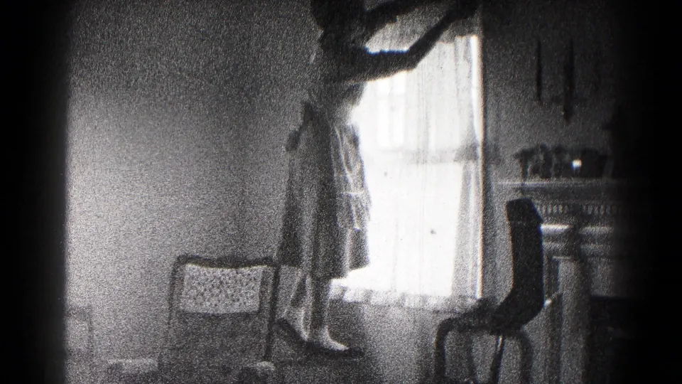 The final frame shows the woman at the bright curtained window, surrounded by dark chairs and a small table in a private interior.