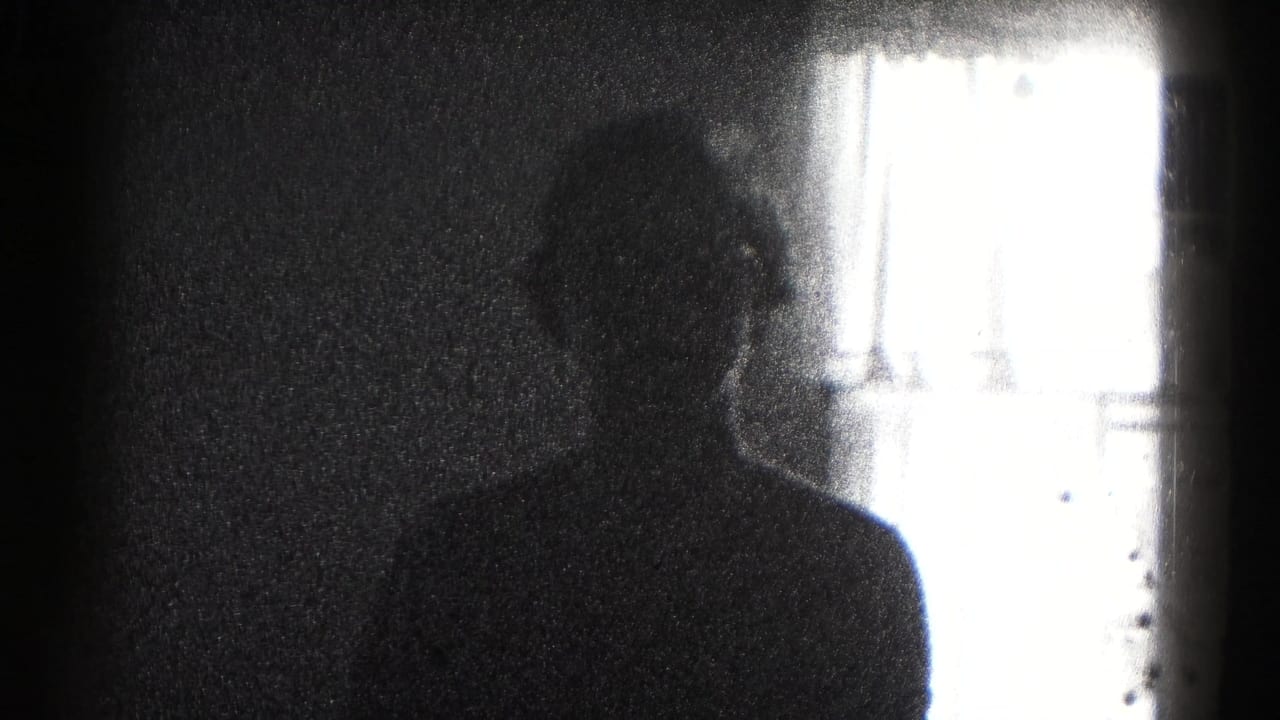 Silhouetted woman stands beside a bright window in a dark interior.