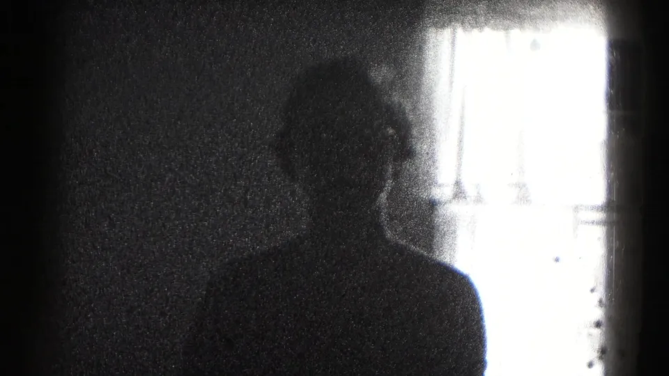 In a 1959 Hagerstown home-movie frame, a silhouetted woman stands in a dim room beside strong window glare.