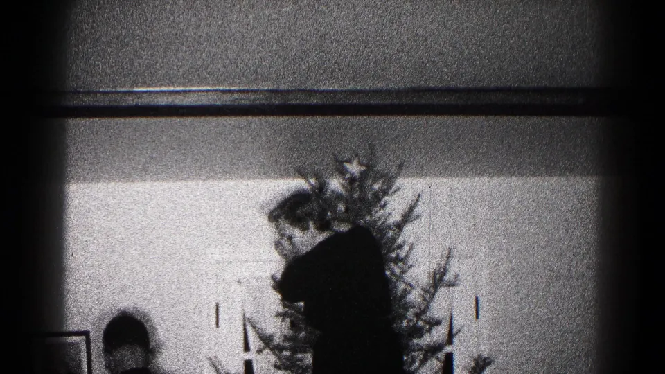 1959 Hagerstown home-movie frame showing a silhouetted adult and child beside a decorated Christmas tree in a private interior.