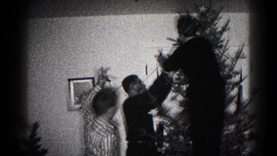 Family members in a 1959 Hagerstown interior appear to place decorations on a Christmas tree, seen in grainy black-and-white 8mm footage.