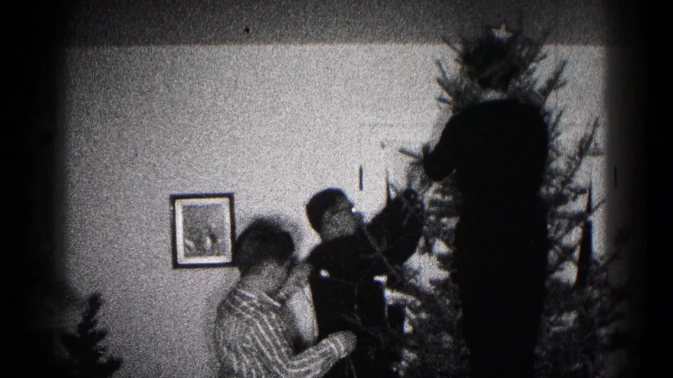 A child in a patterned shirt and two adults stand beside a Christmas tree in this 1959 Hagerstown family home-movie frame.