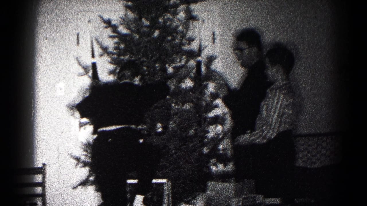 In a 1959 Hagerstown home-movie frame, two people stand near a Christmas tree while arranging decorations in a private room.