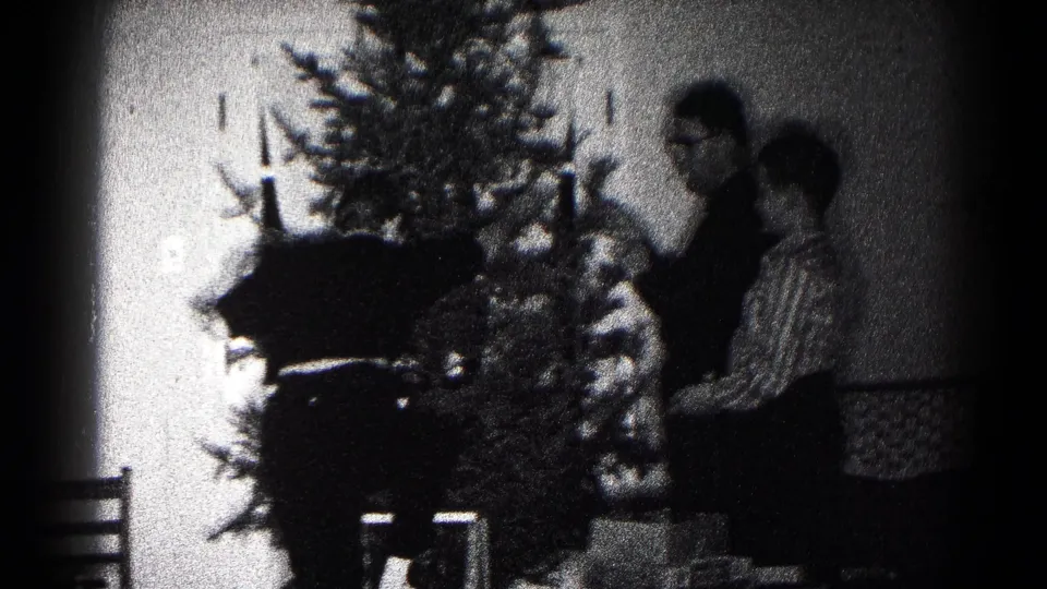 In a 1959 Hagerstown home-movie frame, two people stand near a Christmas tree while arranging decorations in a private room.