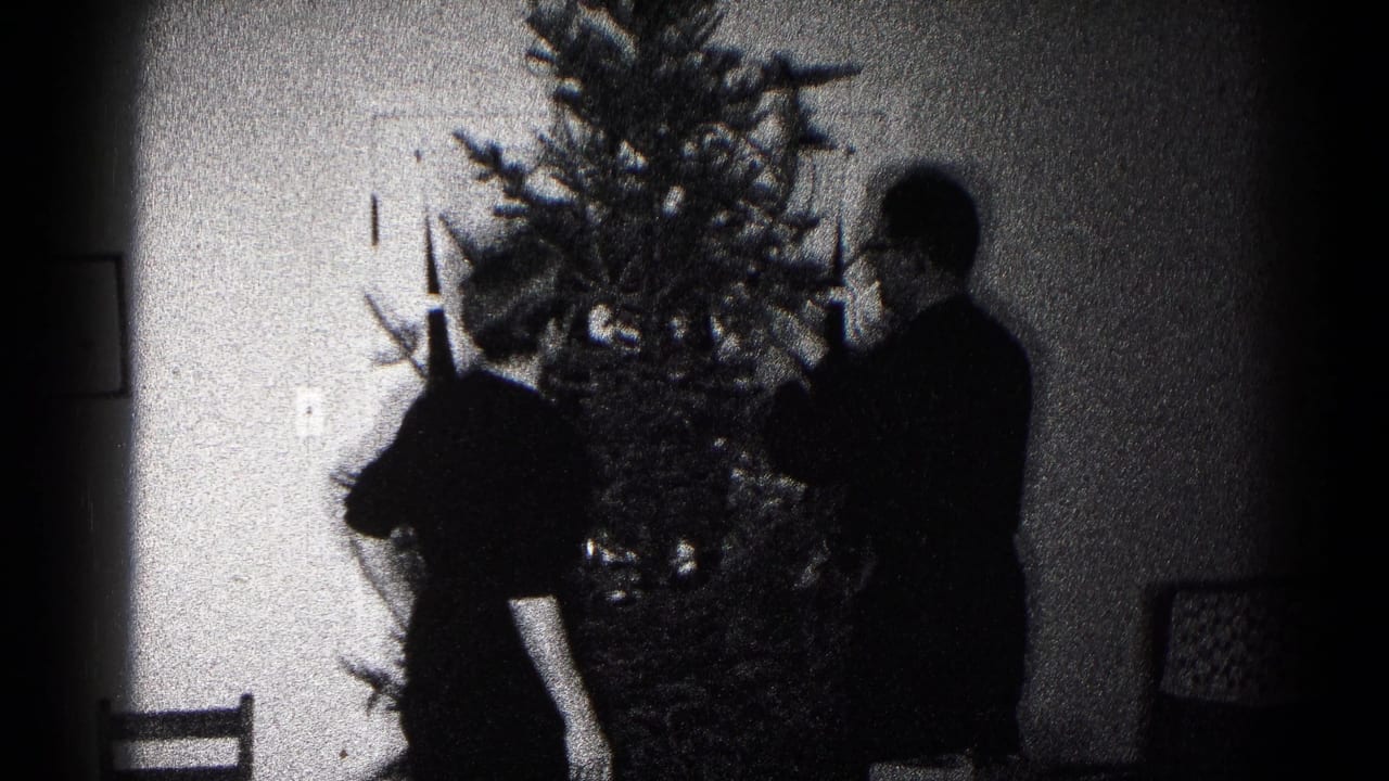 A person bends near the lower branches of a Christmas tree as another person stands nearby in the 1959 Hagerstown interior.