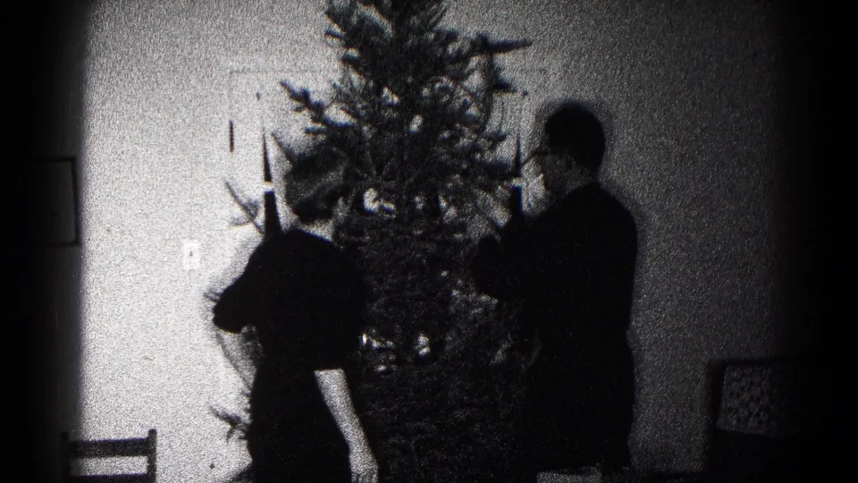A person bends near the lower branches of a Christmas tree as another person stands nearby in the 1959 Hagerstown interior.