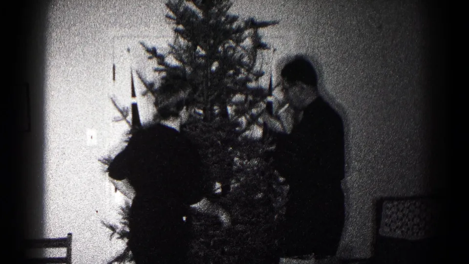 A person in dark clothing stands close to the Christmas tree, likely adjusting decorations, in the 1959 Hagerstown home-movie scene.