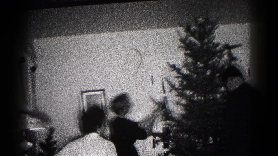 A grainy 1959 Hagerstown living-room frame shows a person decorating a Christmas tree while another figure sits nearby.