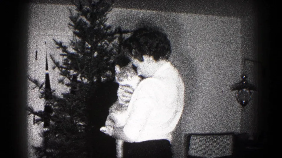 In 1959 Hagerstown home-movie footage, a woman stands beside a small Christmas tree while holding a cat in a dim interior.