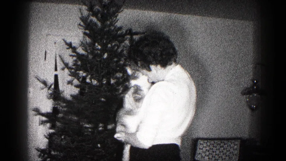 Black-and-white 8mm frame from Hagerstown, Maryland, showing a woman holding a cat close to a small Christmas tree.