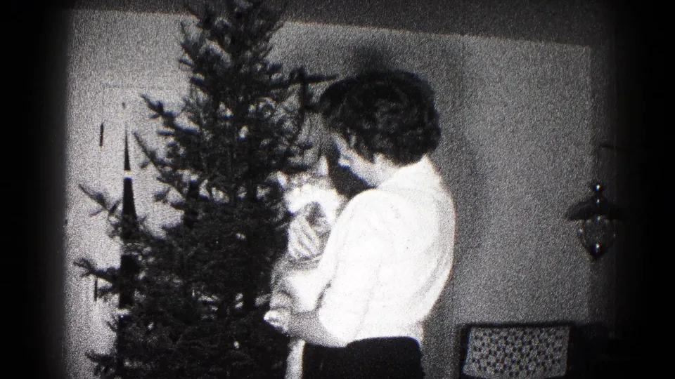 A woman in a light blouse holds a cat beside a Christmas tree in grainy 1959 Maryland home-movie footage.