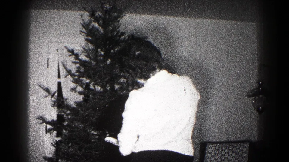Soft, overexposed 8mm frame shows the woman bending or turning near the Christmas tree inside the Hagerstown home.
