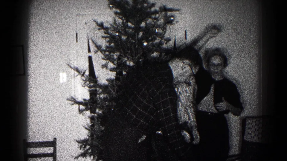 1959 Hagerstown home-movie frame showing three family members gathered beside an indoor Christmas tree during decorating.