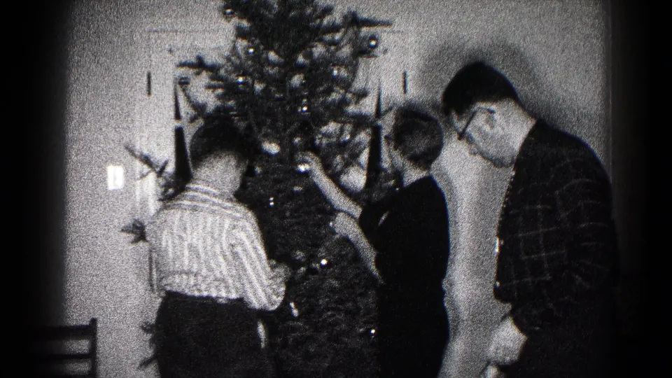 Black-and-white 8mm frame from the Hagerstown holiday interior, with family members reaching toward the Christmas tree.