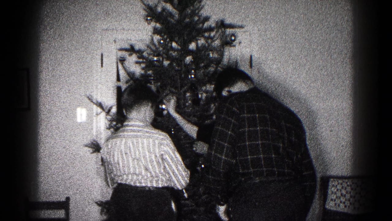 Home-movie frame showing family members close to the tree, adjusting ornaments in a private Hagerstown interior.
