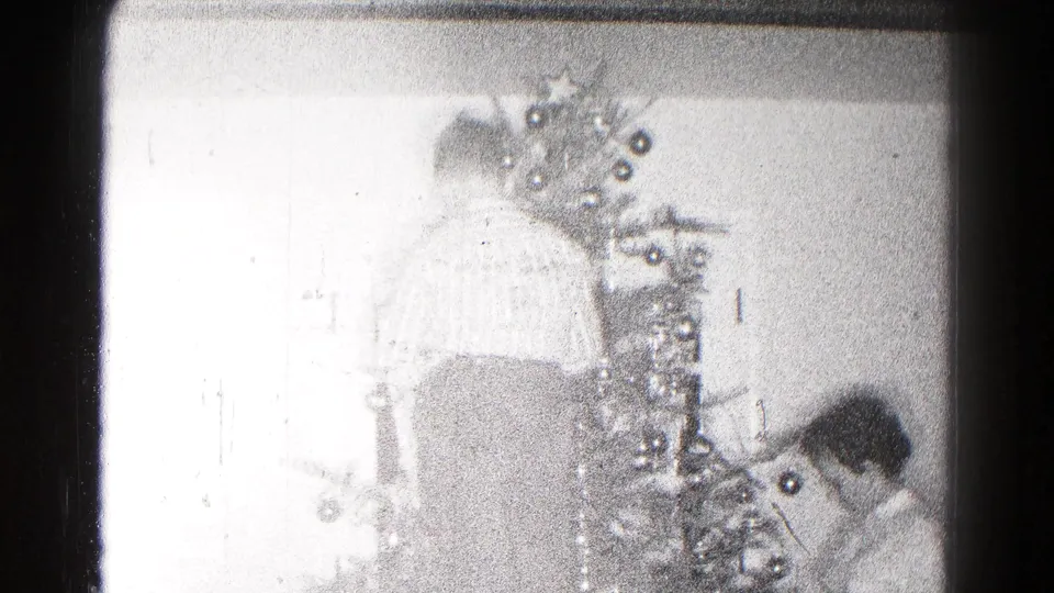 Bright home-movie frame of a decorated Christmas tree and a person near the base inside a private 1959 Hagerstown home.