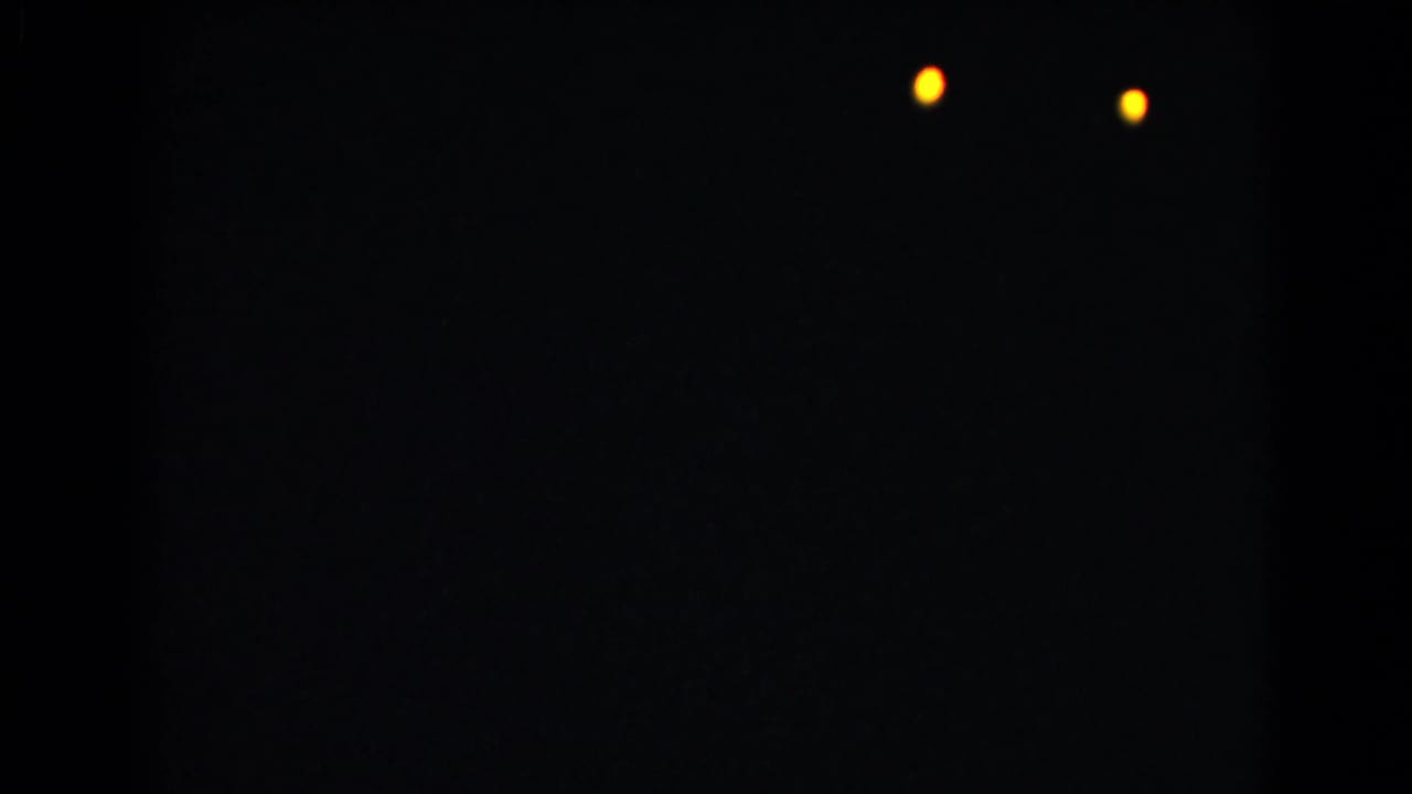 A mostly dark 8mm frame from the Christmas home movie shows two small warm lights against a black field.