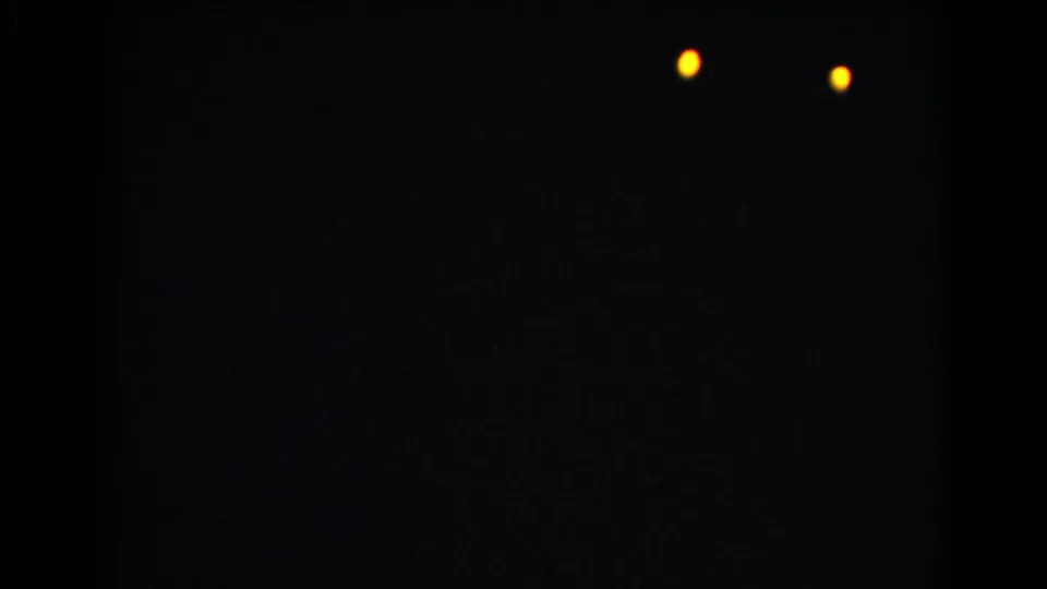 A mostly dark 8mm frame from the Christmas home movie shows two small warm lights against a black field.