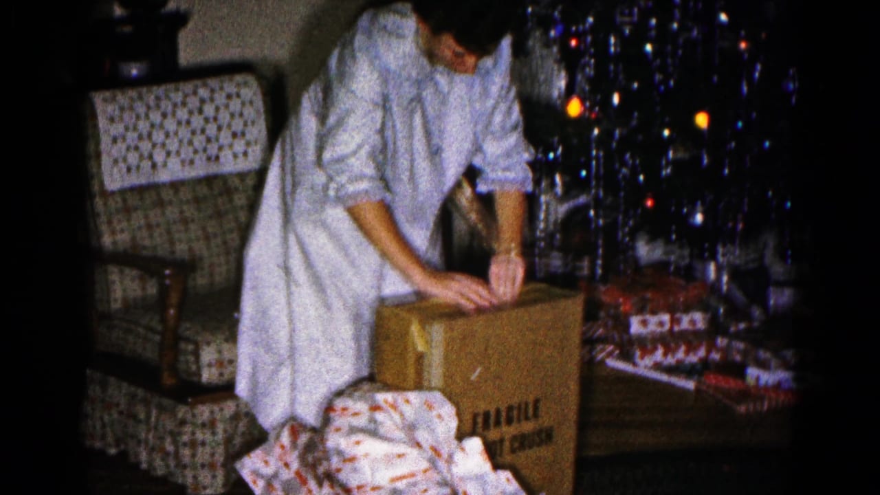 A woman in light pajamas opens a FRAGILE cardboard box in a 1959 Hagerstown Christmas living room scene.