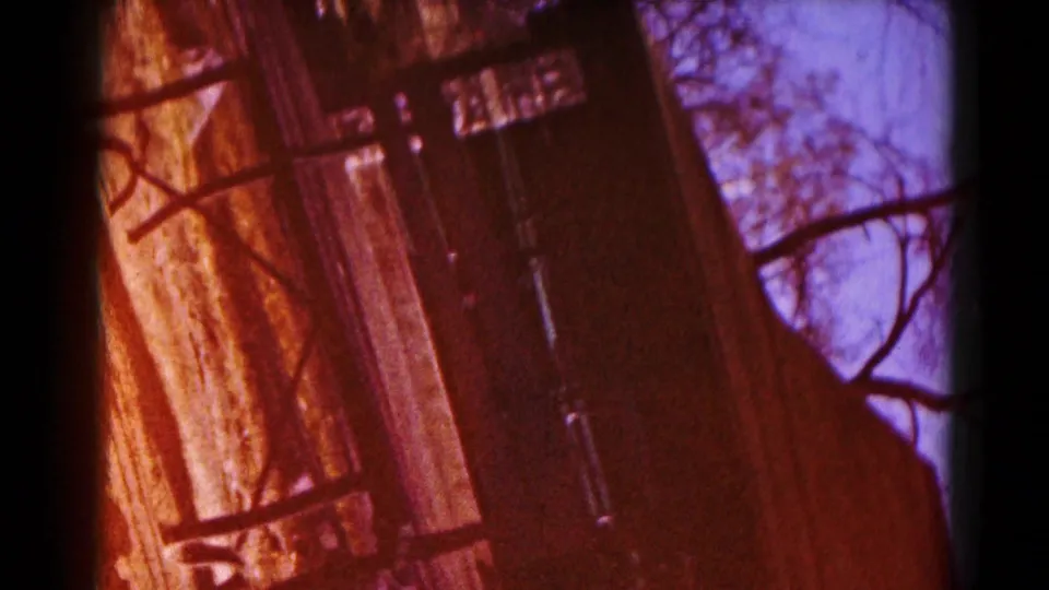 1959 Hagerstown home-movie frame with a tilted view of a small wooden park structure among trees and blue sky.