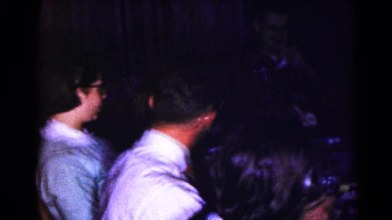 1959 Hagerstown home-movie frame showing adults gathered at a dimly lit dinner table during conversation.
