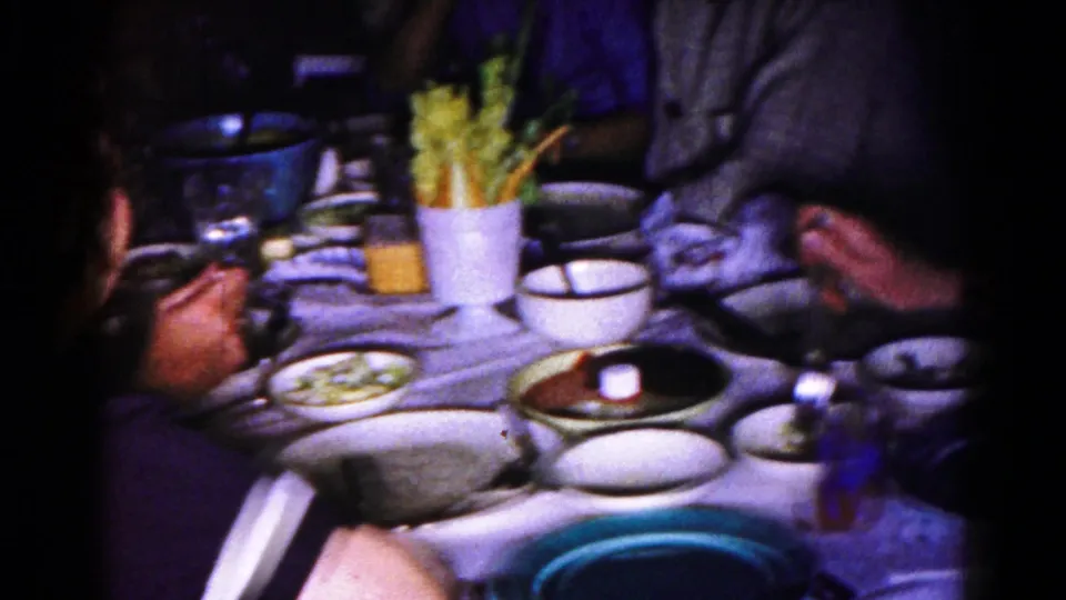 Close 1959 Hagerstown home-movie view of a family dinner table with dishes, glasses, and seated adults.