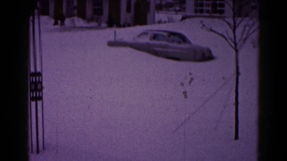 Final 1959 Hagerstown frame of a snow-buried sedan on a quiet residential street, bordered by bare trees, houses, and visible 8mm film edges.