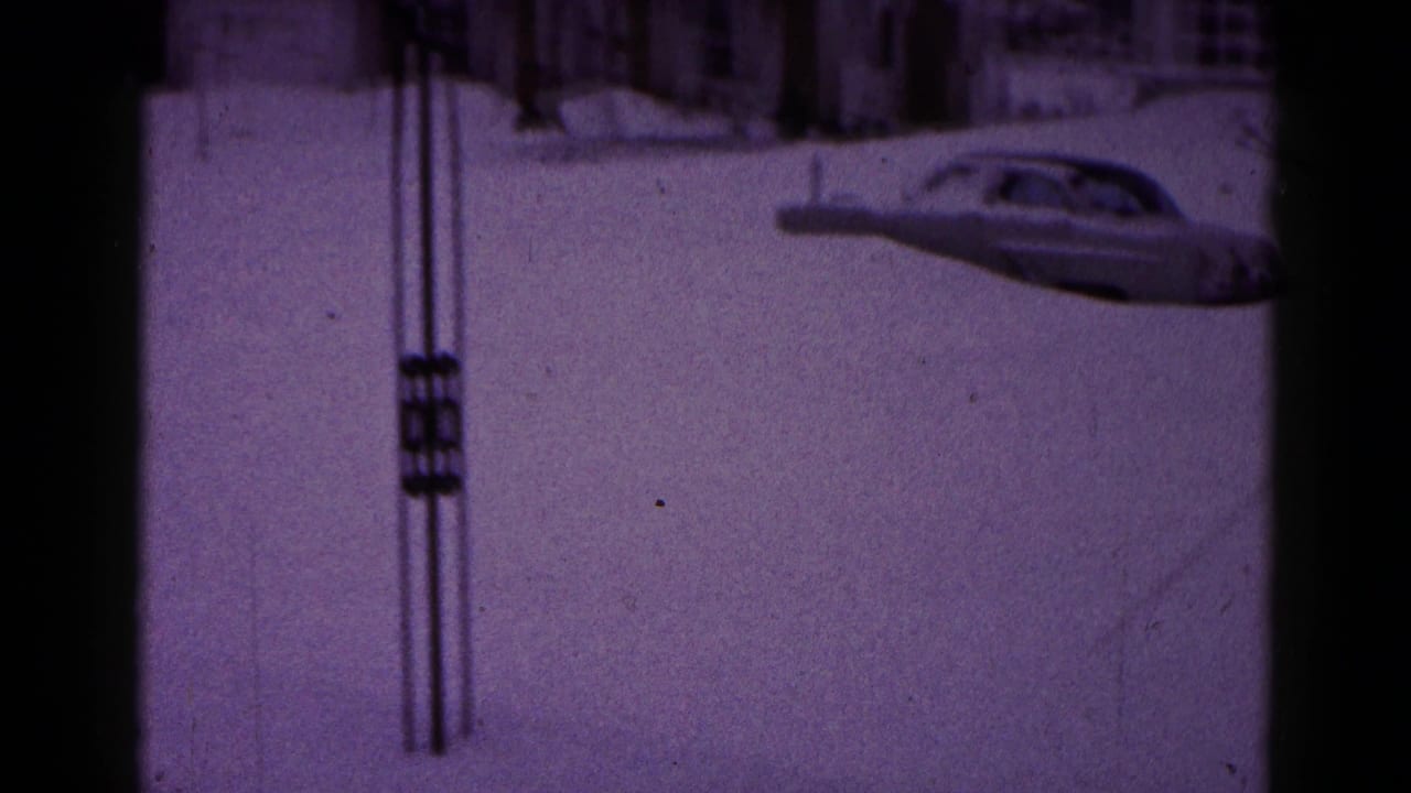 Snow-covered residential road with a partially buried car and utility poles.