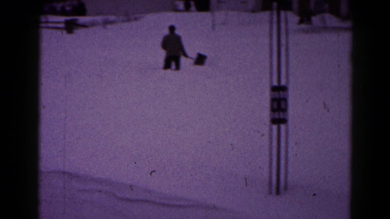 1959 Hagerstown frame showing a bundled man shoveling or carrying snow near utility poles in a snow-covered residential area.