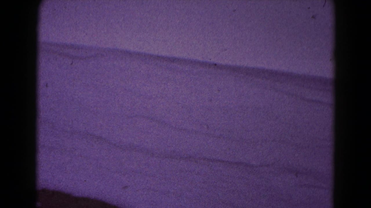 Soft purple-tinted 8mm frame of snowy terrain or an open winter slope, likely from the Hagerstown home-movie clip.